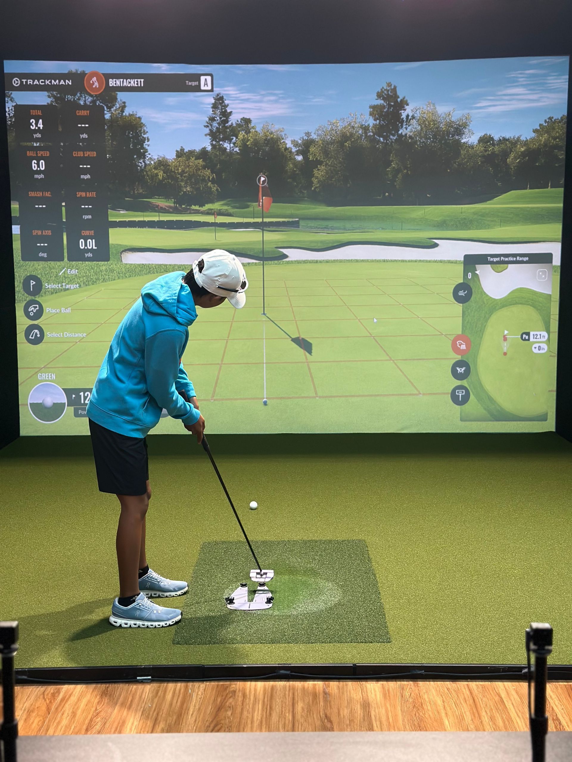Golfer in a blue jacket lining up a putt indoors on a golf simulator screen with a green fairway backdrop