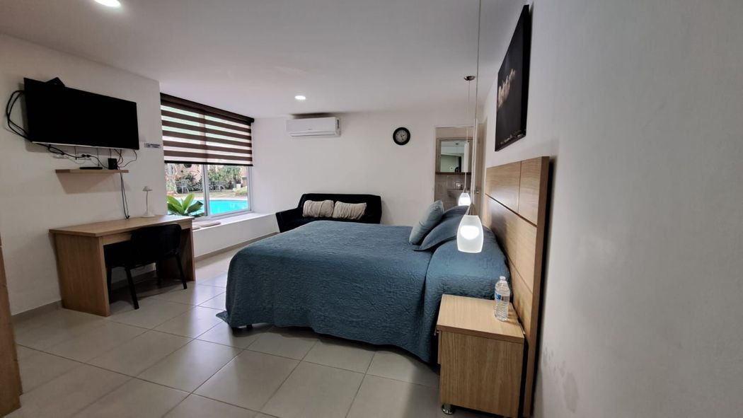 Habitación de hotel con dos camas, escritorio, televisor de pared, aire acondicionado y ventana con persianas a rayas.