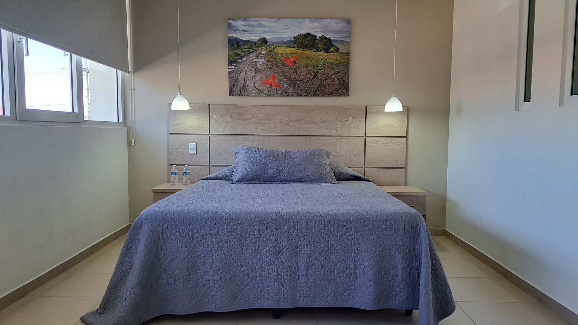Cama bien hecha en un dormitorio minimalista con ropa de cama azul, lámparas de pared 