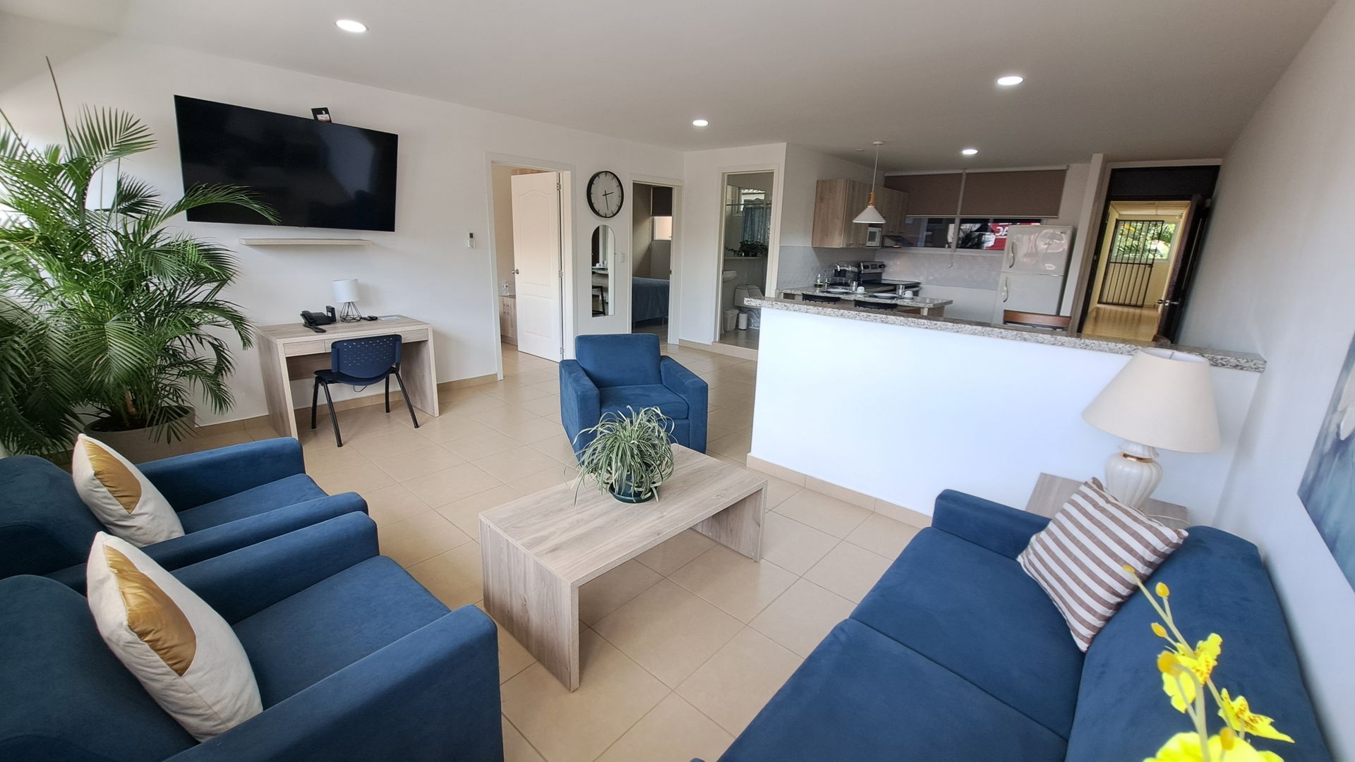 Luminoso salón diáfano con sofás azules, mesa de centro, televisor y barra de cocina.