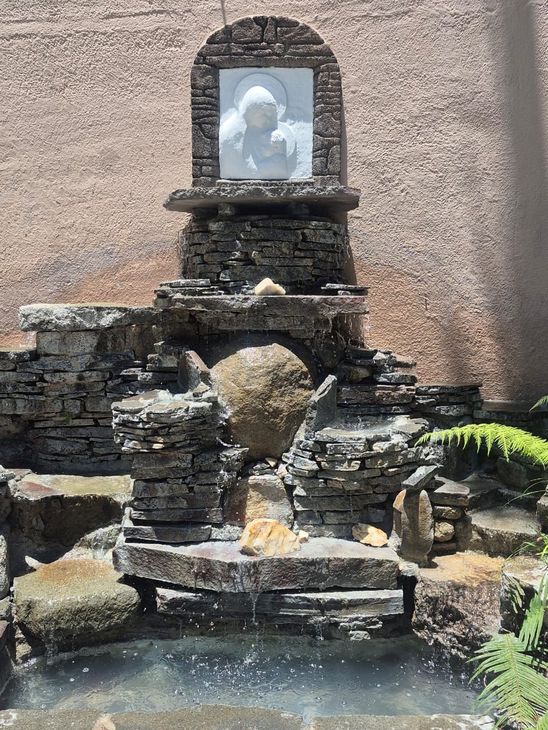 Fuente de jardín de piedra con una pequeña estatua en un nicho, agua que fluye hacia un estanque.