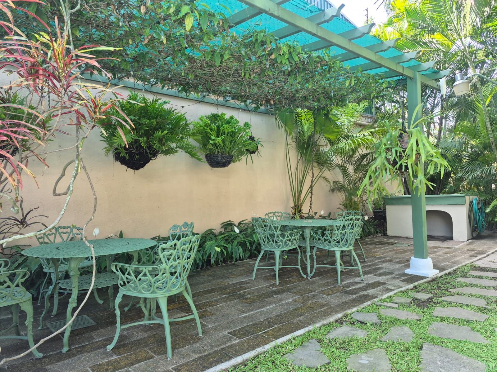 Patio exterior cubierto con mesas y sillas de metal de color verde menta, plantas colgantes 