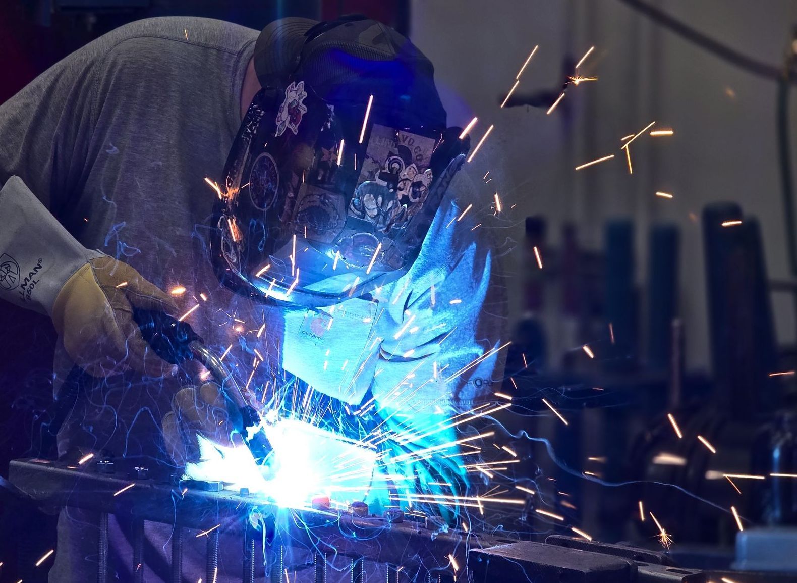 Welder in protective gear creating bright blue sparks on metal in a workshop