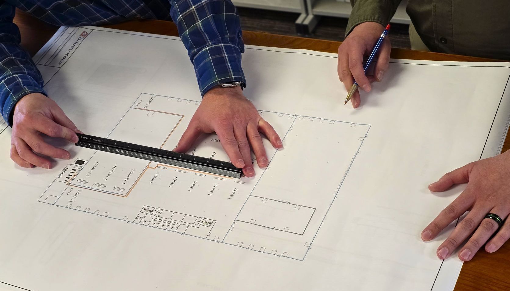 Hands measuring a paper floor plan with a ruler on a table.