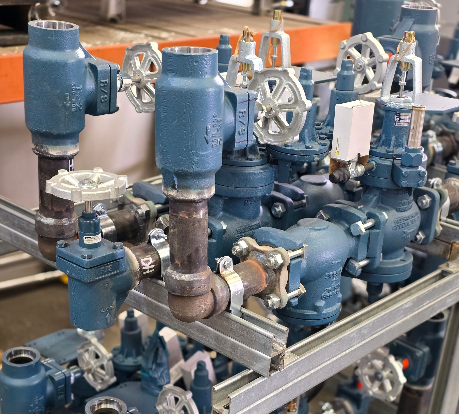 Blue industrial pipe valve assembly on a metal frame in a workshop or factory setting