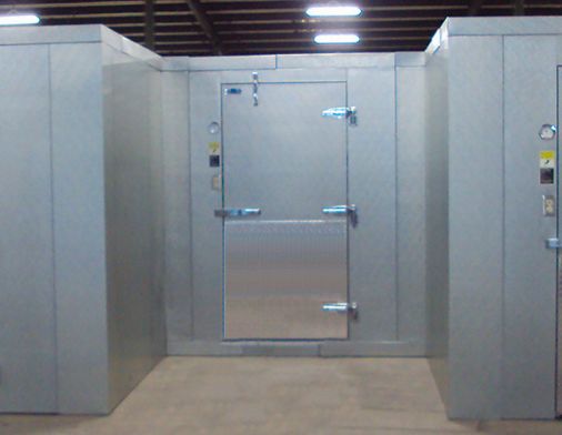 Stainless steel walk-in freezer door between metal wall panels in an industrial room