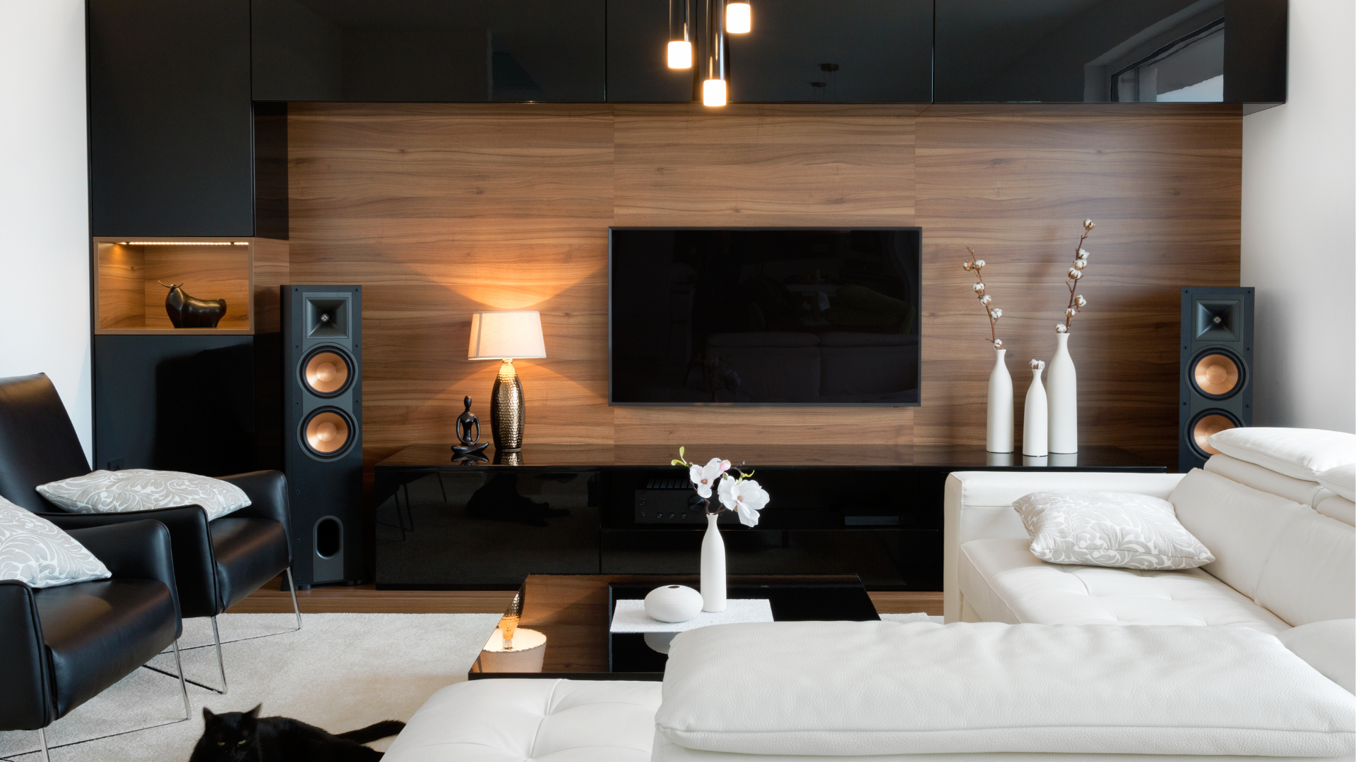 A living room with a couch , chair , speakers and a flat screen tv.