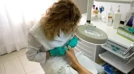 Professionista odontoiatrico con camice bianco e guanti color ottanio al lavoro sul piede di un paziente