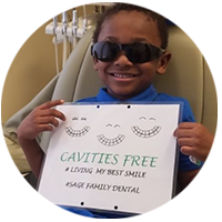 A young boy wearing sunglasses is holding a sign that says cavities free