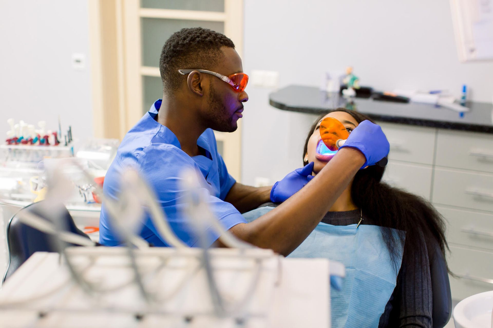 Dentist in blue scrubs treating a patient in a dental clinic, with tools and equipment in the foreground.