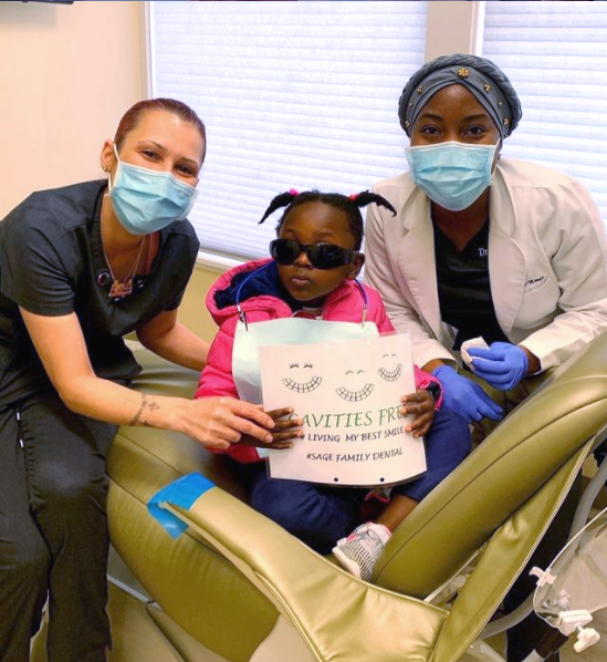 A little girl is sitting in a dental chair holding a sign that says 