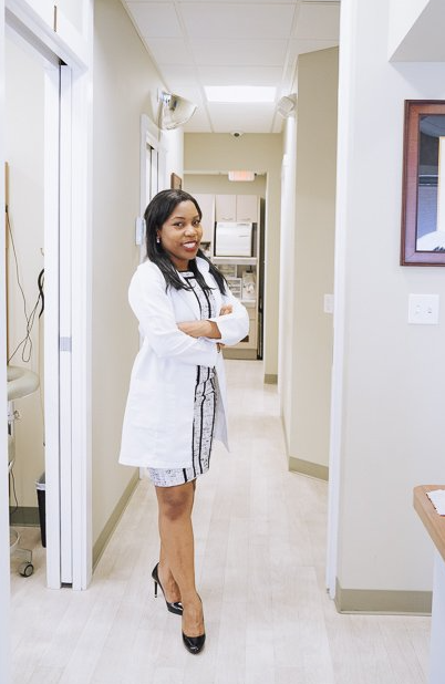 A woman in a lab coat is standing in a hallway with her arms crossed.