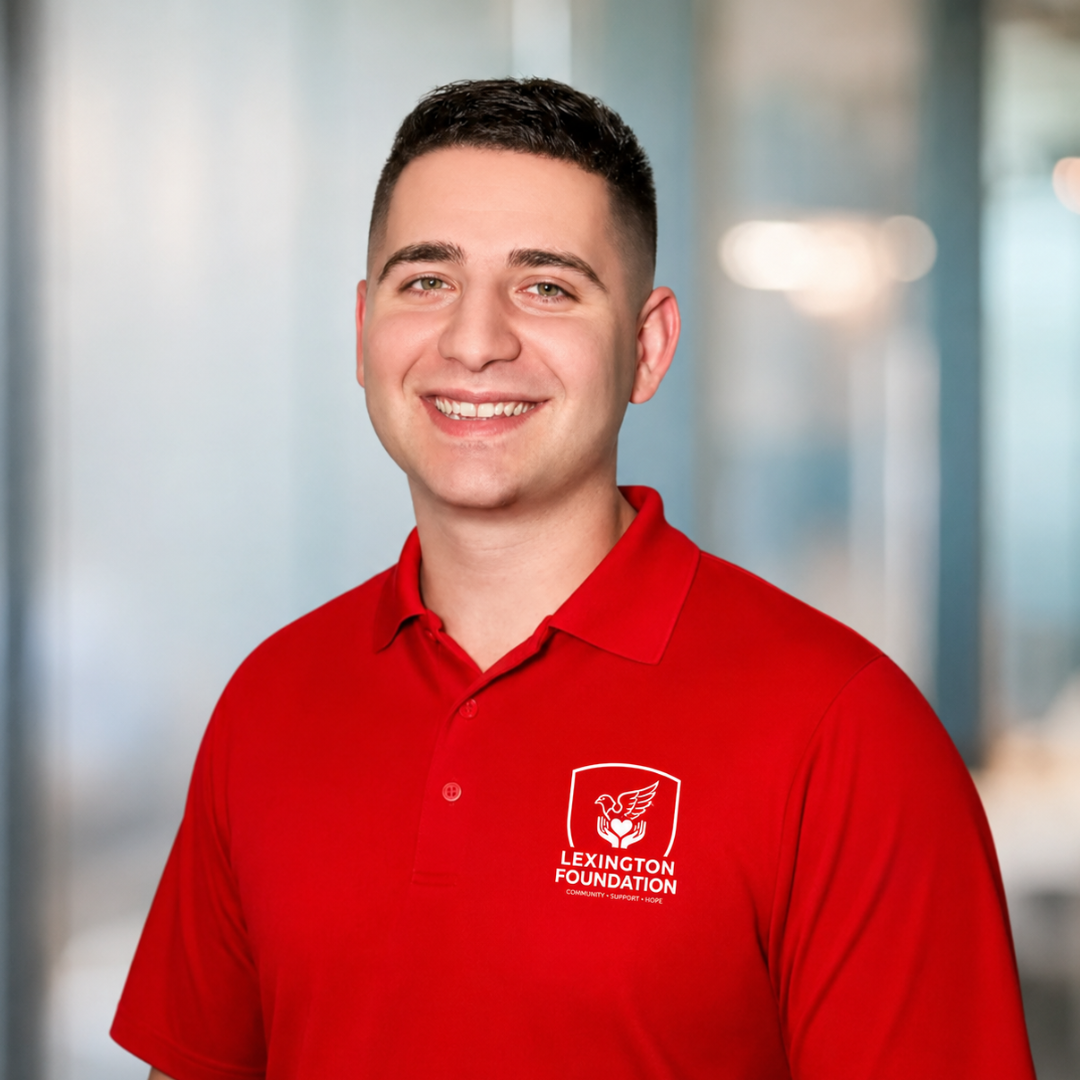 Man in red polo shirt with Lexington Clinic logo smiling at the camera. White sleeves, blurred background.
