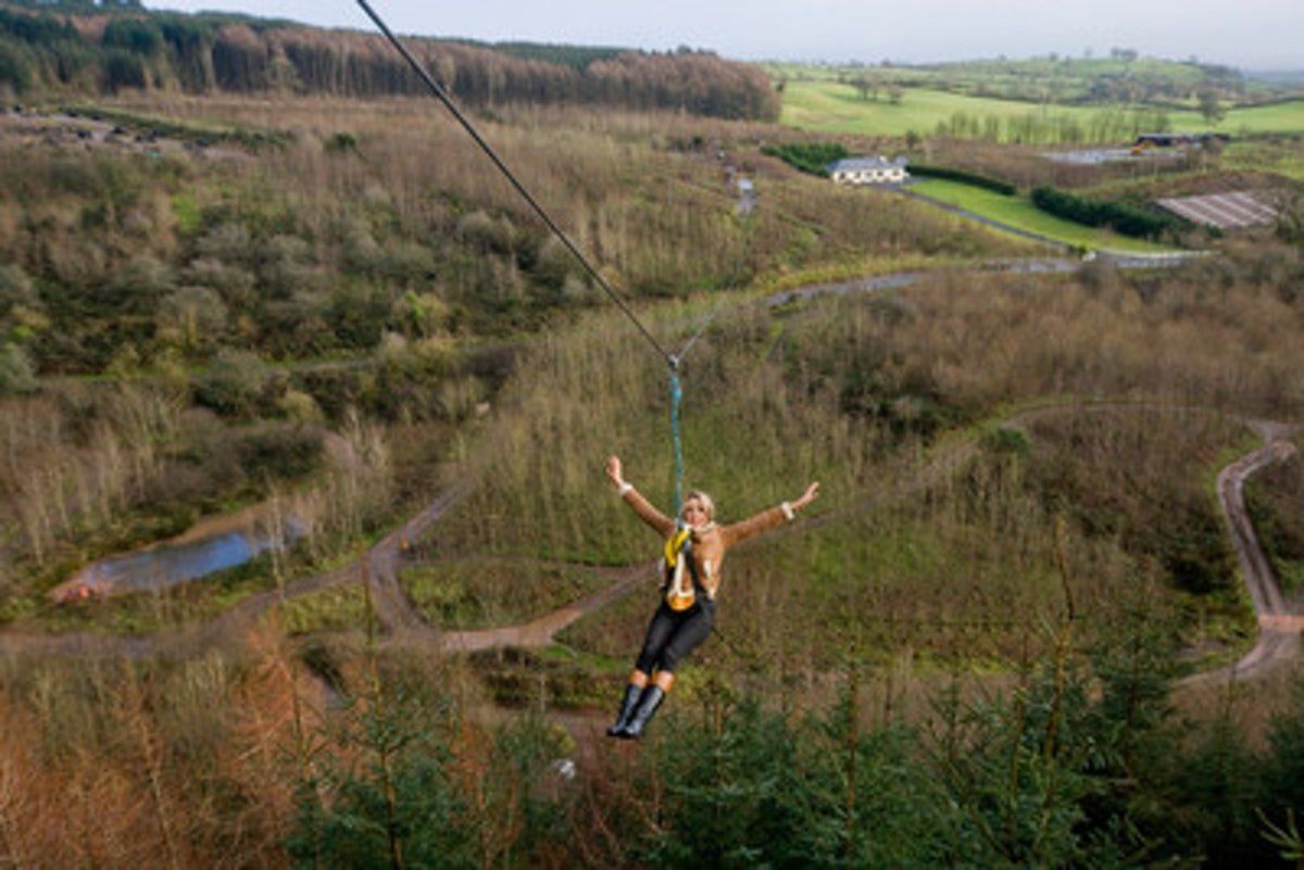 Person ziplining over a wooded landscape with fields and ponds below