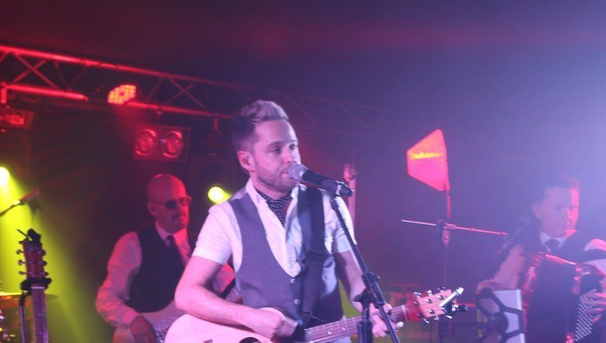 Singer performing onstage with a guitar under pink and purple concert lights