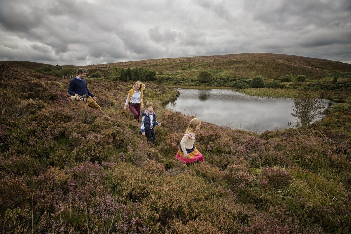 People hiking through heather near a small lake under cloudy skies