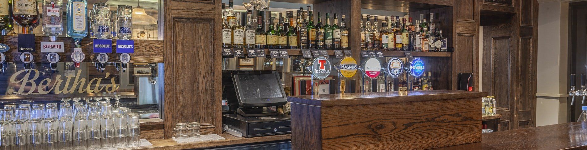 Bar shelves and taps inside a warmly lit pub, with a wooden counter and glass display cases