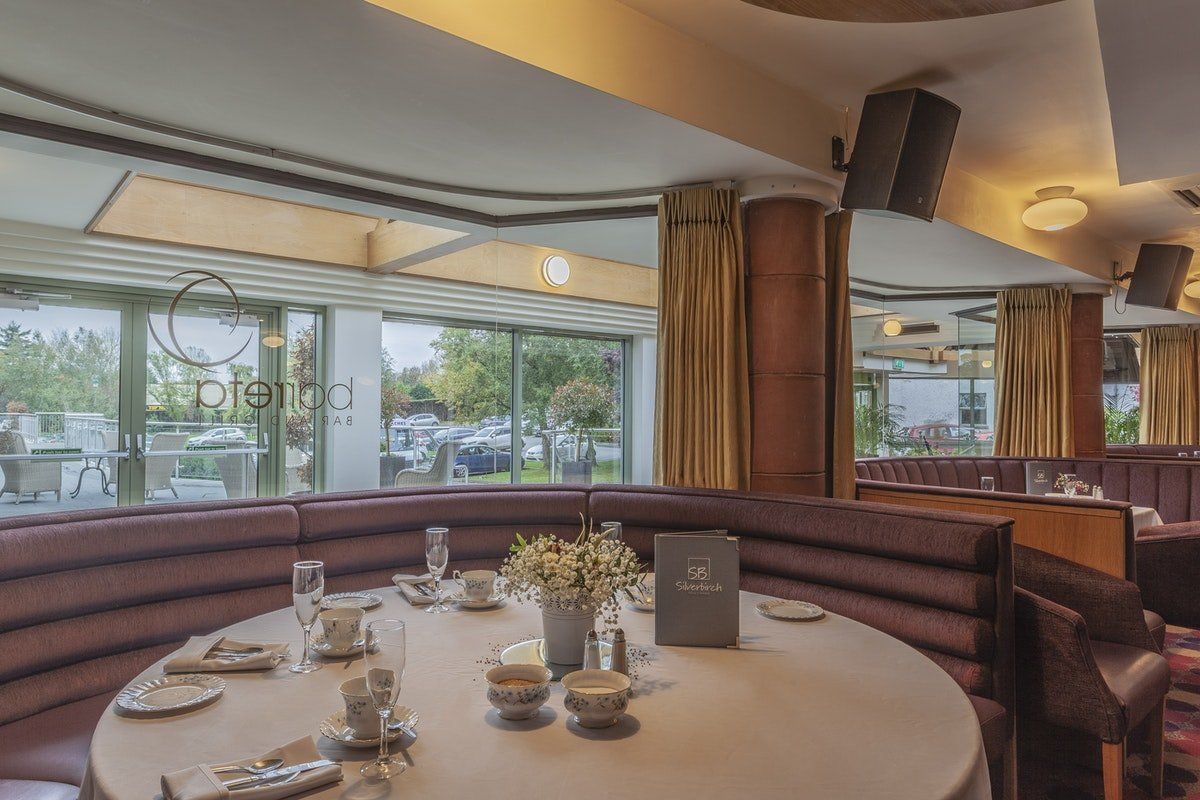 Elegant restaurant booth with a round table set for dining by large windows and soft lighting