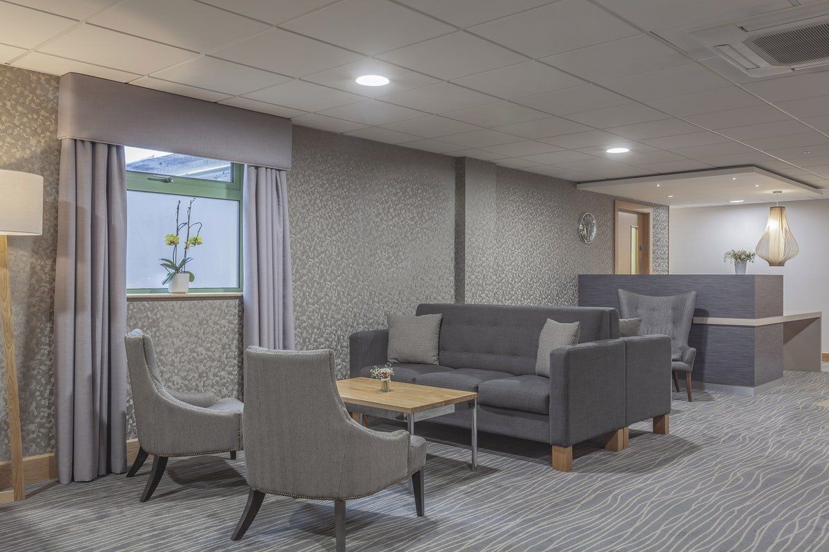 Modern lounge with gray sofas, chairs, and a small table beside a window and wall decor.