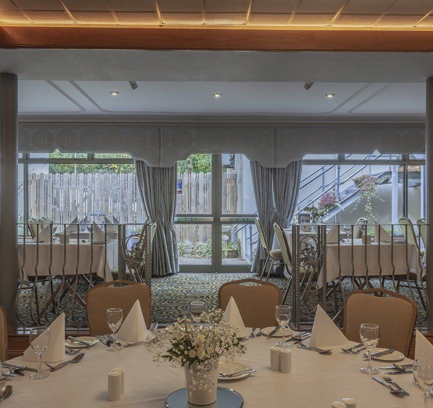 Elegant banquet hall with set round tables, folded napkins, and large windows with curtains.