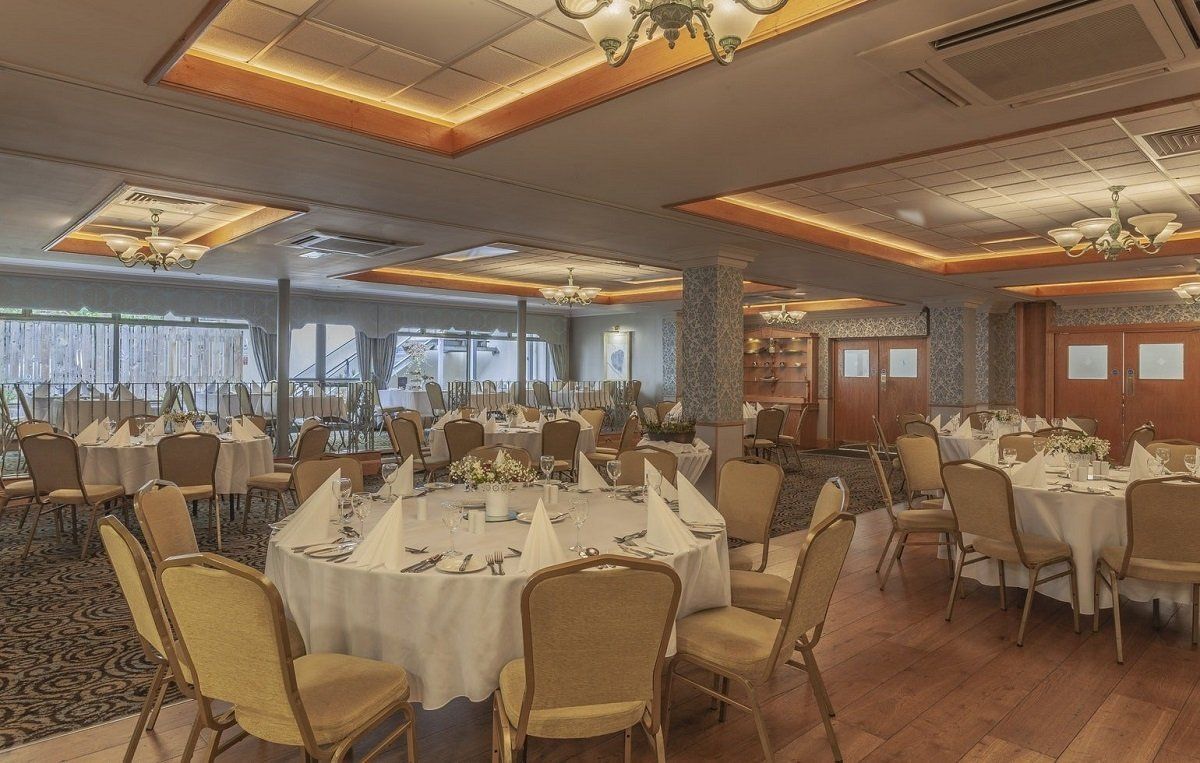 Elegant banquet hall with round, set tables, upholstered chairs, and large windows overlooking the city
