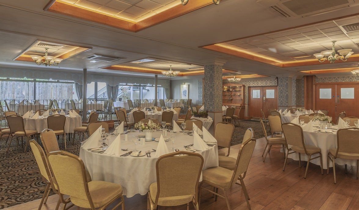 Elegant banquet hall with round tables, cream chairs, and warm ceiling lighting by large windows