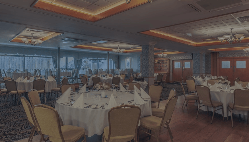 Elegant banquet hall with round tables, white tablecloths, and large windows overlooking the sea.