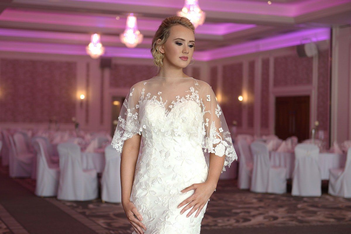 Bride in a white lace wedding dress standing in a pink-lit banquet hall