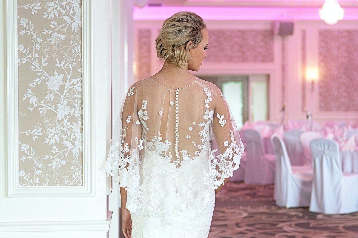 Bride in white gown walking through a pink-lit wedding reception hall