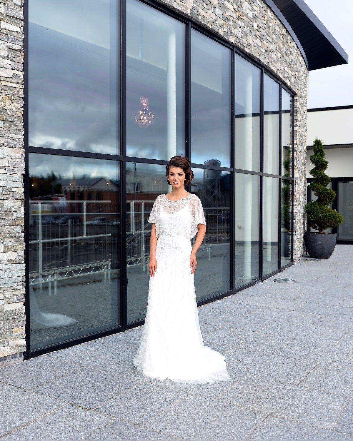 Woman in a white wedding dress standing outside a modern building with large glass windows