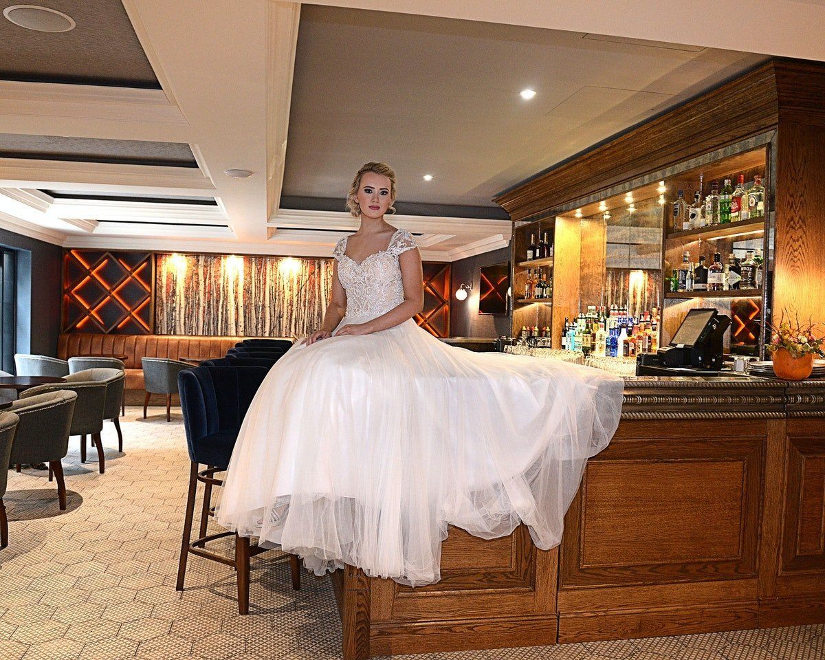 Woman in a white dress standing on a bar counter in a warmly lit lounge.