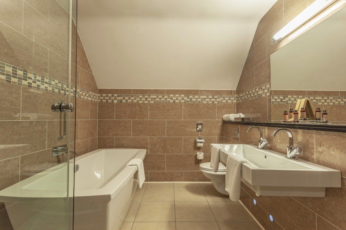 Elegant tiled bathroom with bathtub, two sinks, mirrors, and a long overhead light.