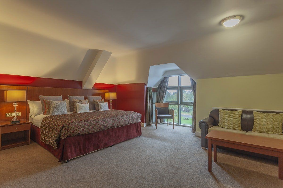 Spacious hotel room with king bed, sofa, and arched window overlooking greenery
