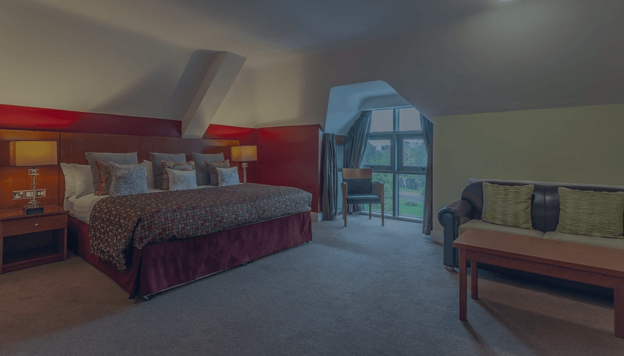 Hotel room with a bed, sofa, nightstands, and a large window view.