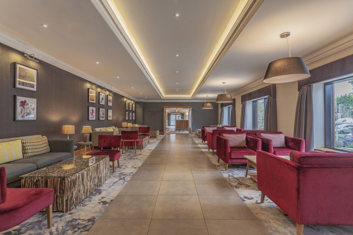 Modern lounge with red chairs, patterned rugs, wall art, and long ceiling lights along a central walkway