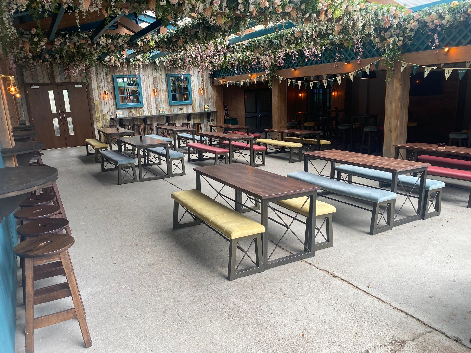Outdoor courtyard with picnic tables and benches under string lights and wooden beams