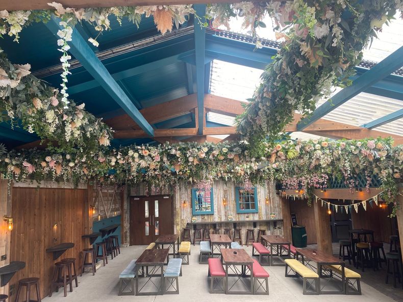 Decorative outdoor seating area with tables, chairs, and flower garlands under a wooden pergola