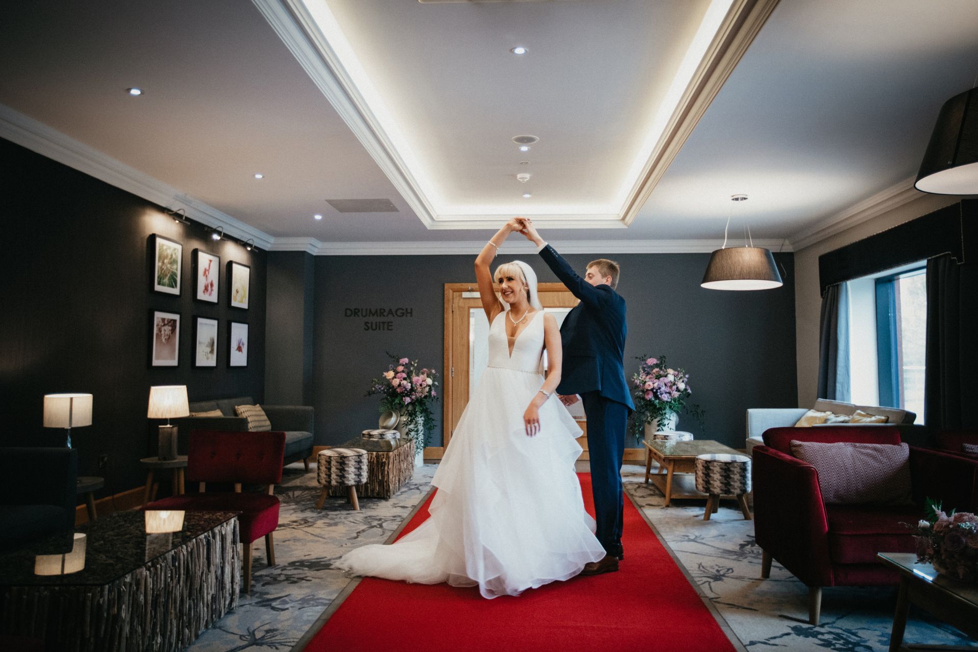 Bride and groom dancing in a hotel lounge under a red carpet and warm ceiling lights