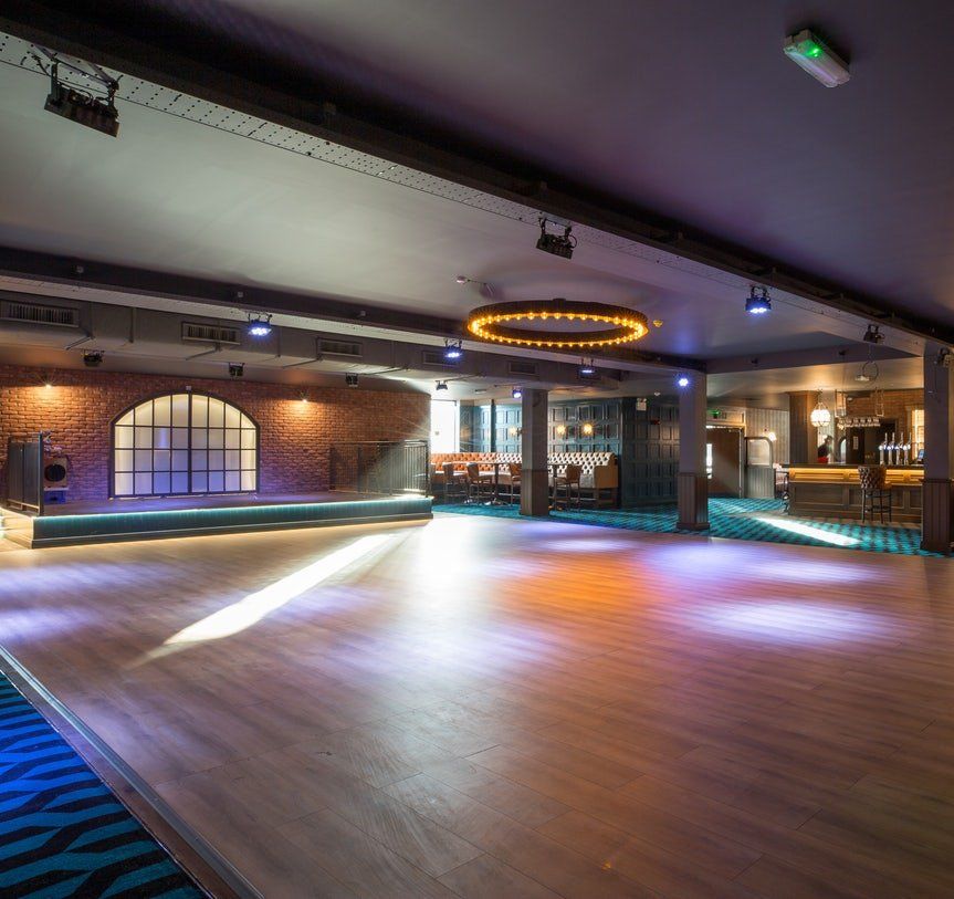 Empty modern dance hall with wood floor, brick walls, and colorful ceiling lights