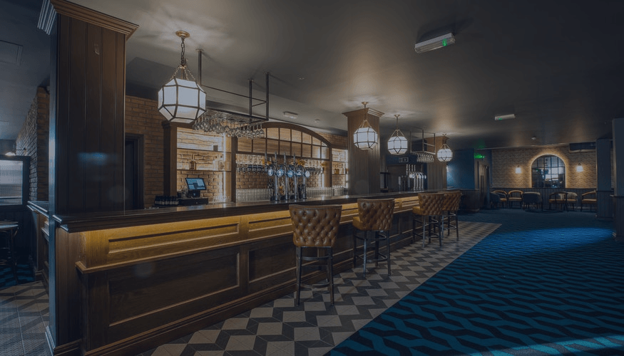Empty bar interior with warm lighting, wooden counters, and blue carpeted seating area