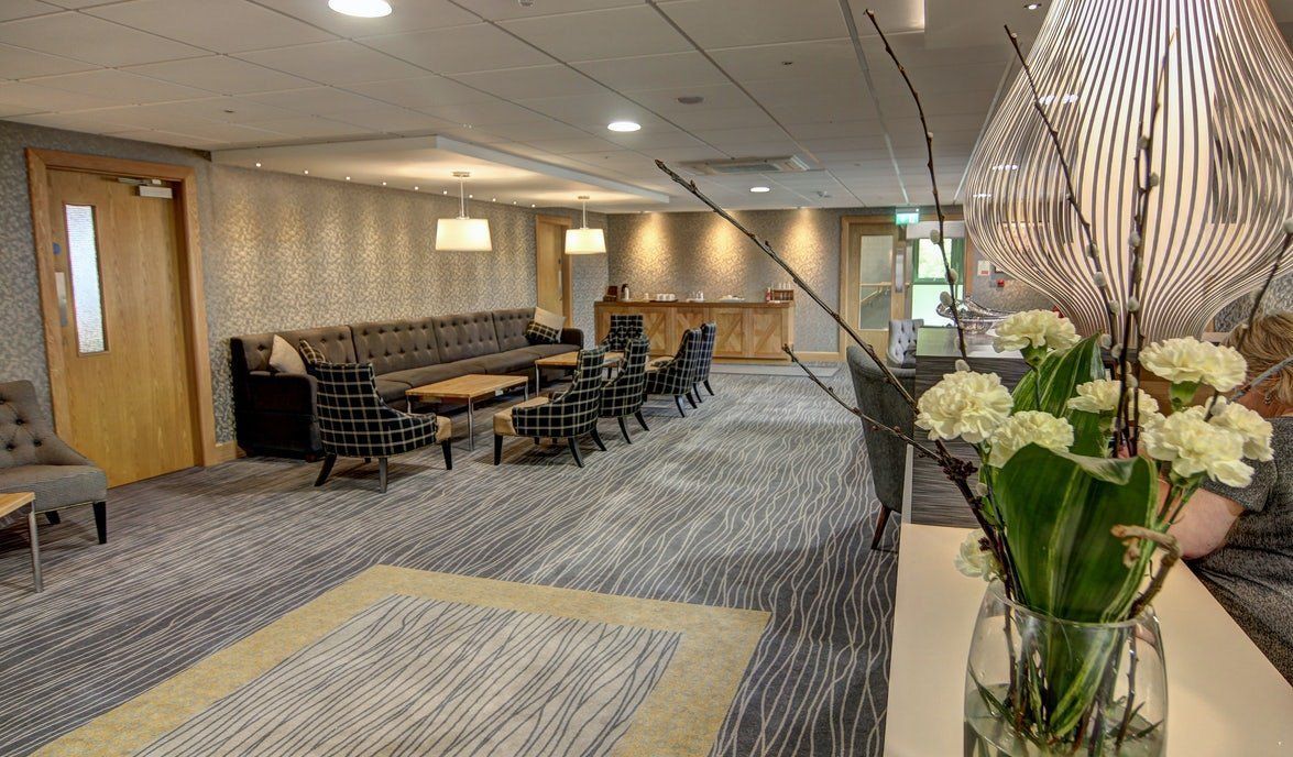 Modern lobby lounge with seating, patterned carpet, and white floral arrangement in the foreground