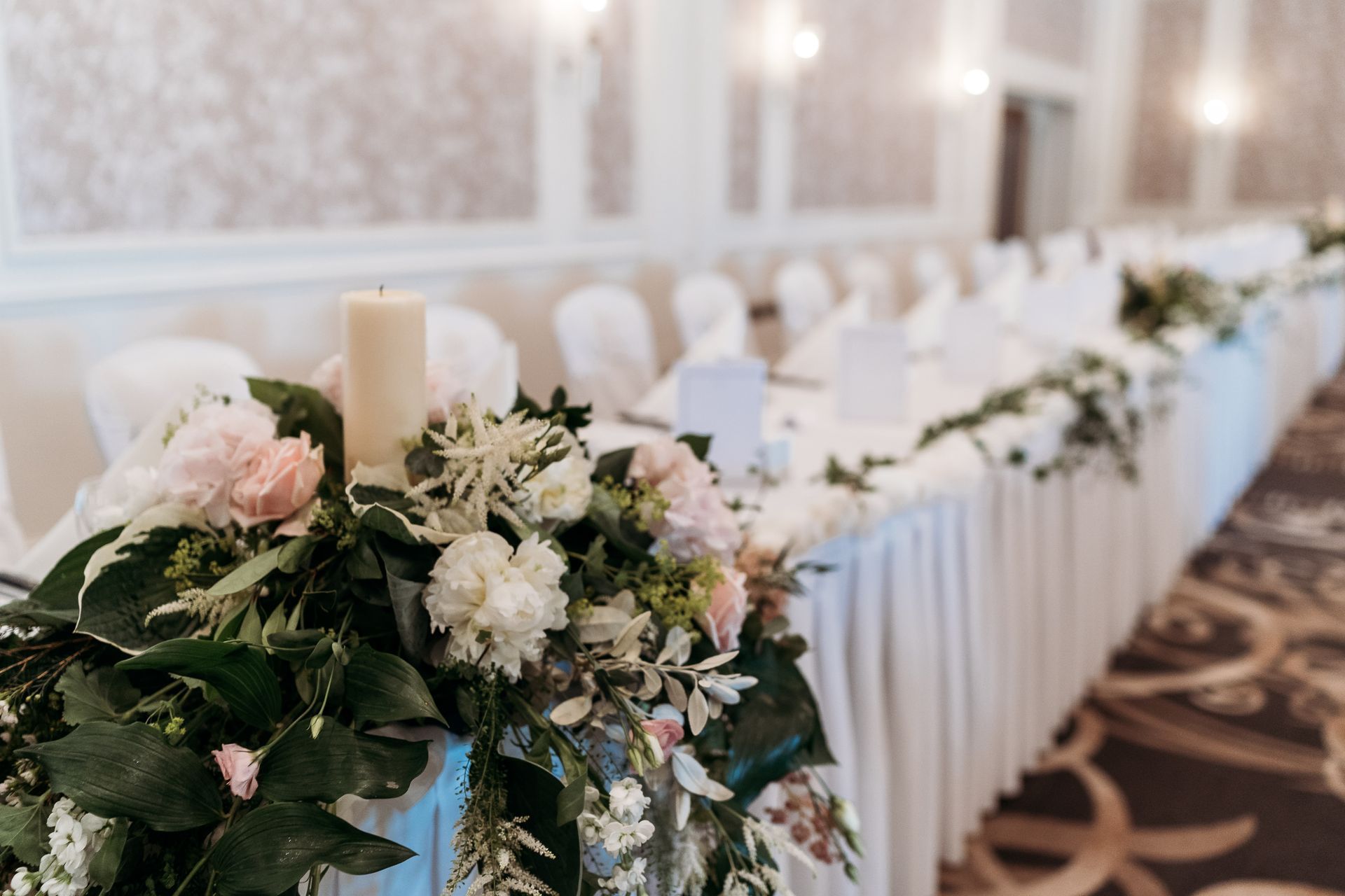Decorated banquet table with white linens and pastel floral centerpieces in a bright reception hall