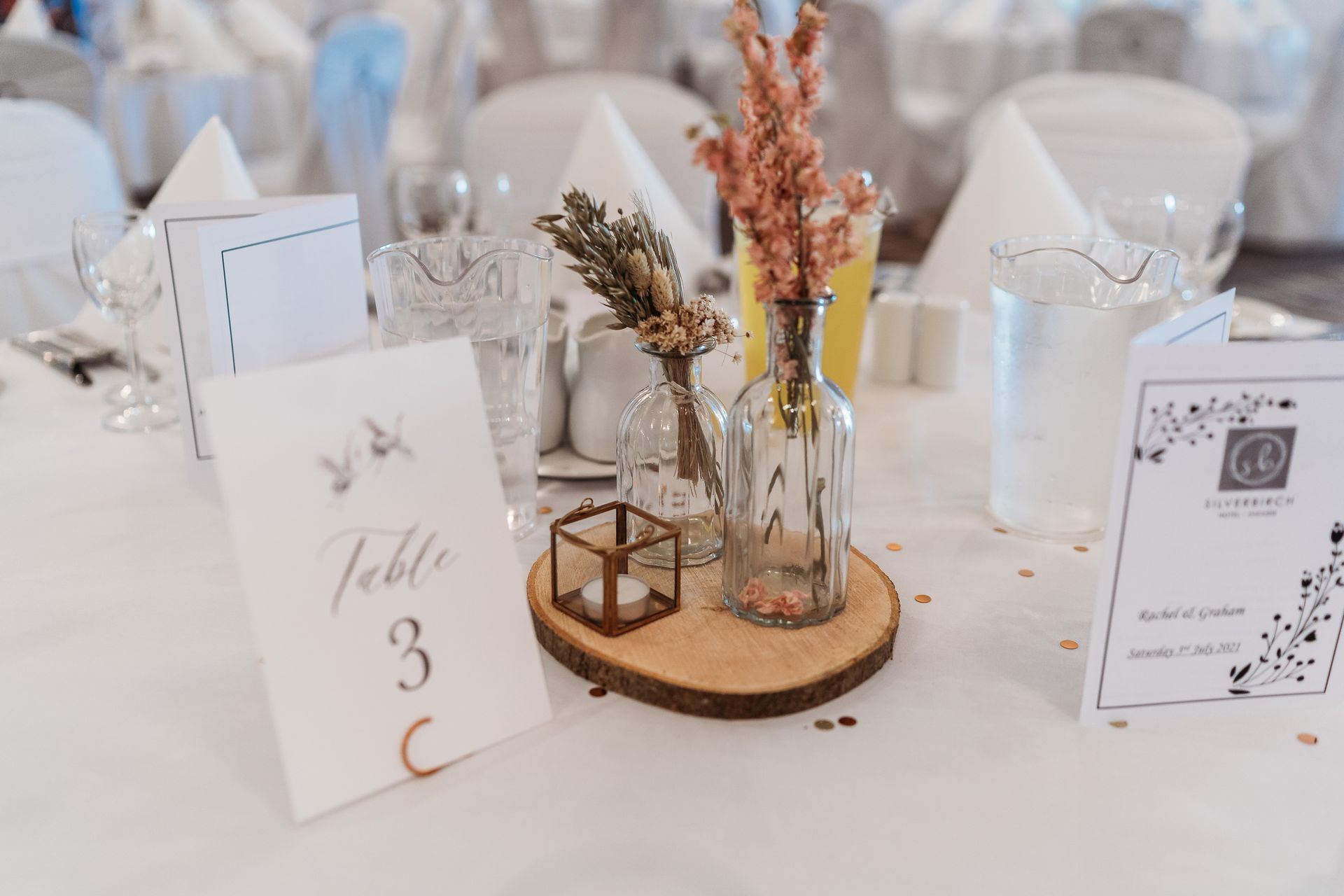 Elegant wedding table centerpiece with dried flowers, candles, and table number 3 on a white tablecloth