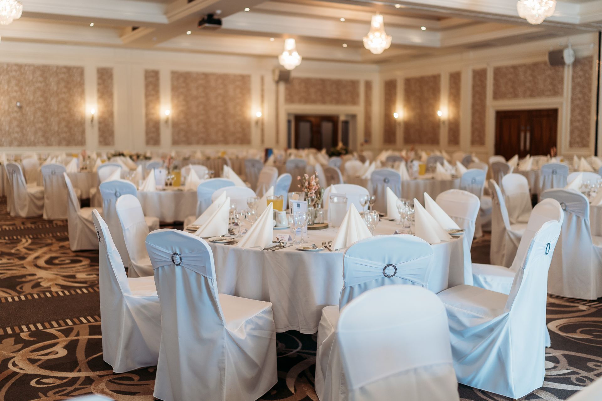 Elegant banquet hall with round tables and white-covered chairs set for an event