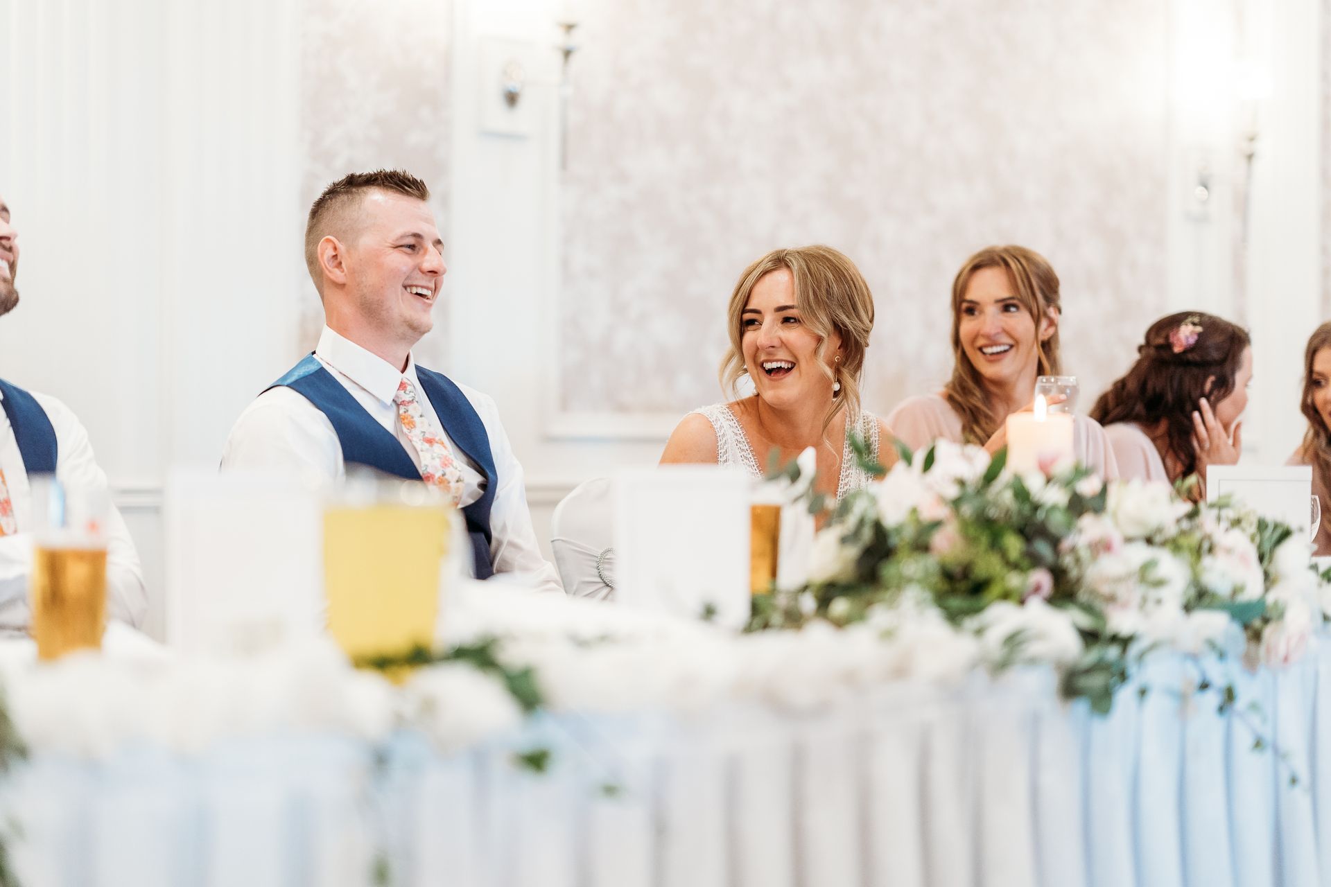 Guests smiling at a wedding reception table with white florals and candles