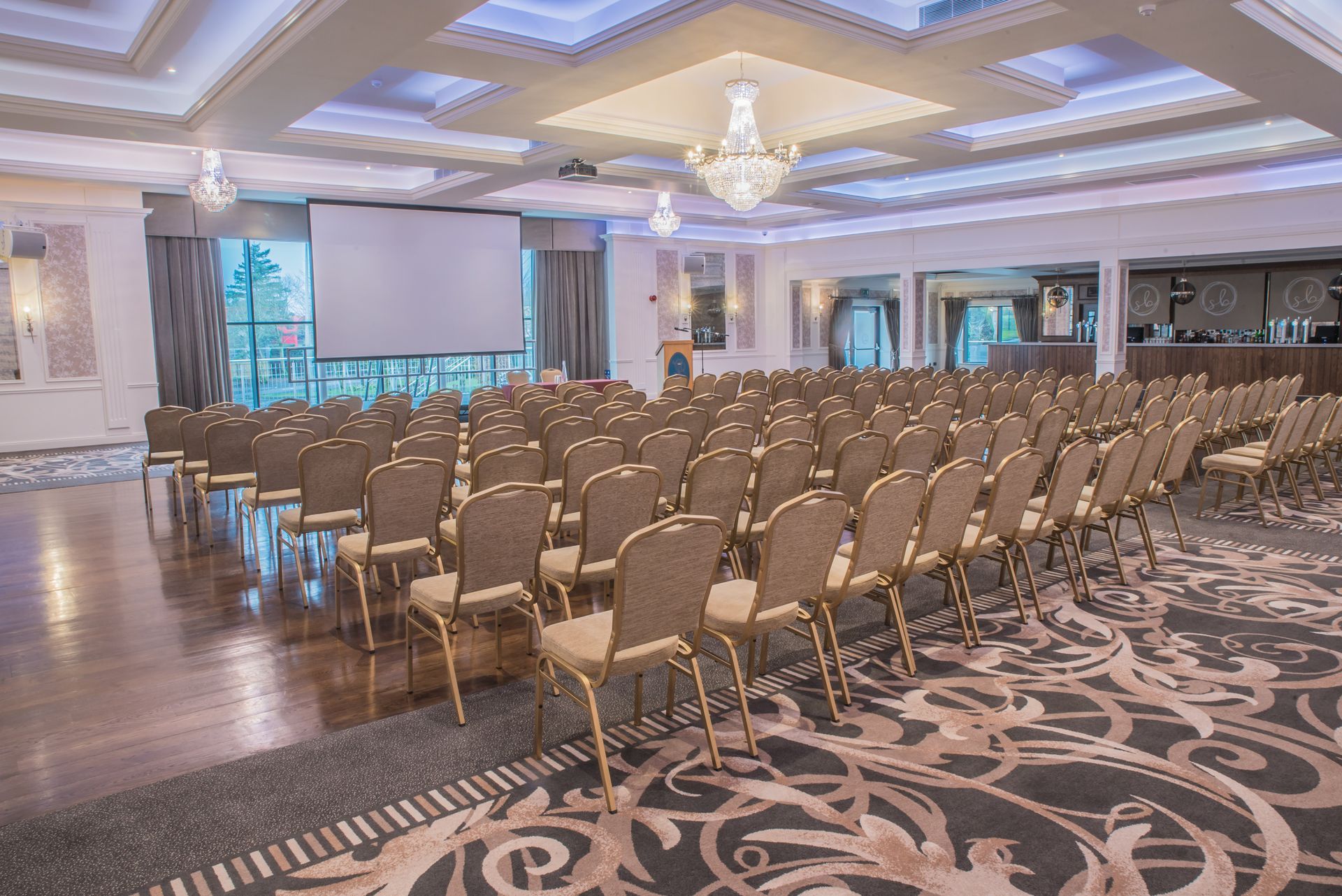 Empty banquet hall with rows of gold chairs, chandelier lighting, and patterned carpet