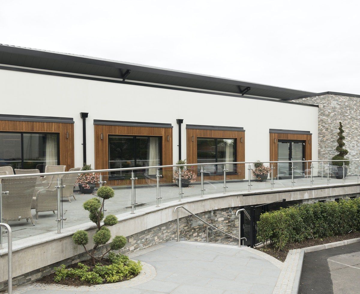 Modern building terrace with glass railing, wooden doors, patio furniture, and landscaped planters