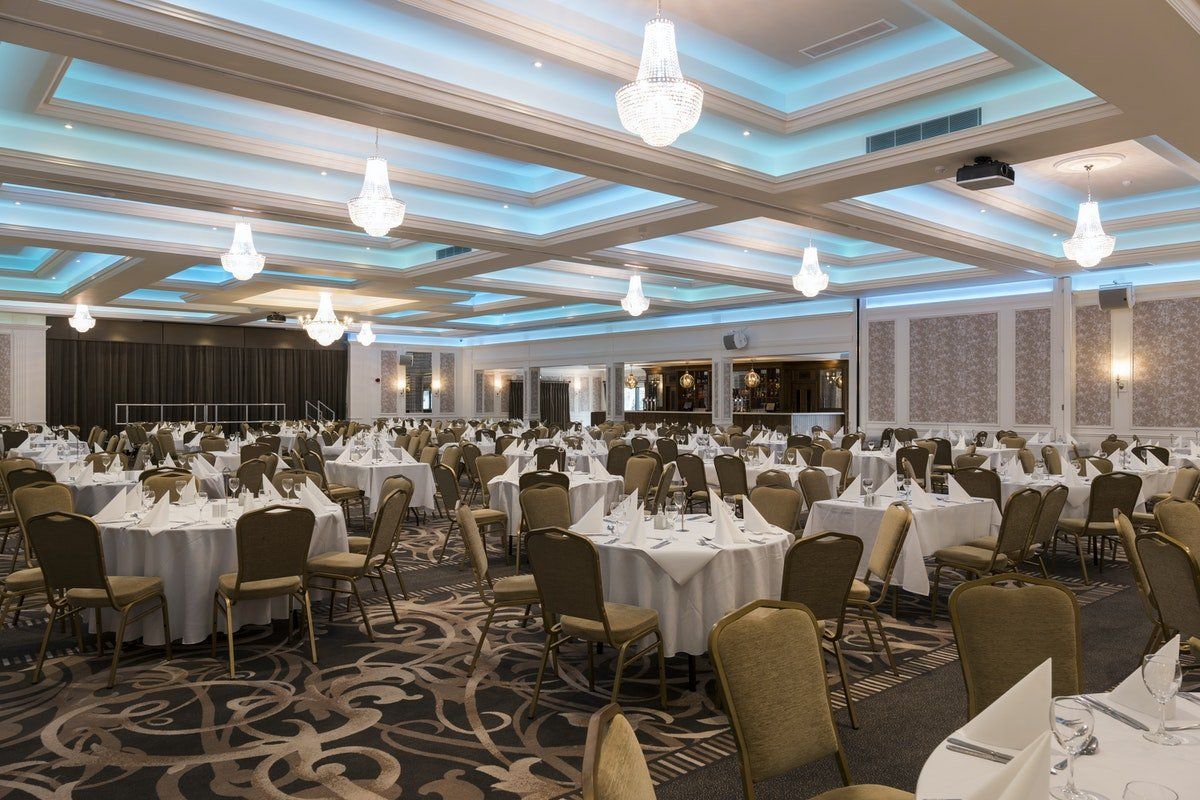 Elegant banquet hall with white tablecloths, chandeliers, and patterned carpet set for a formal event