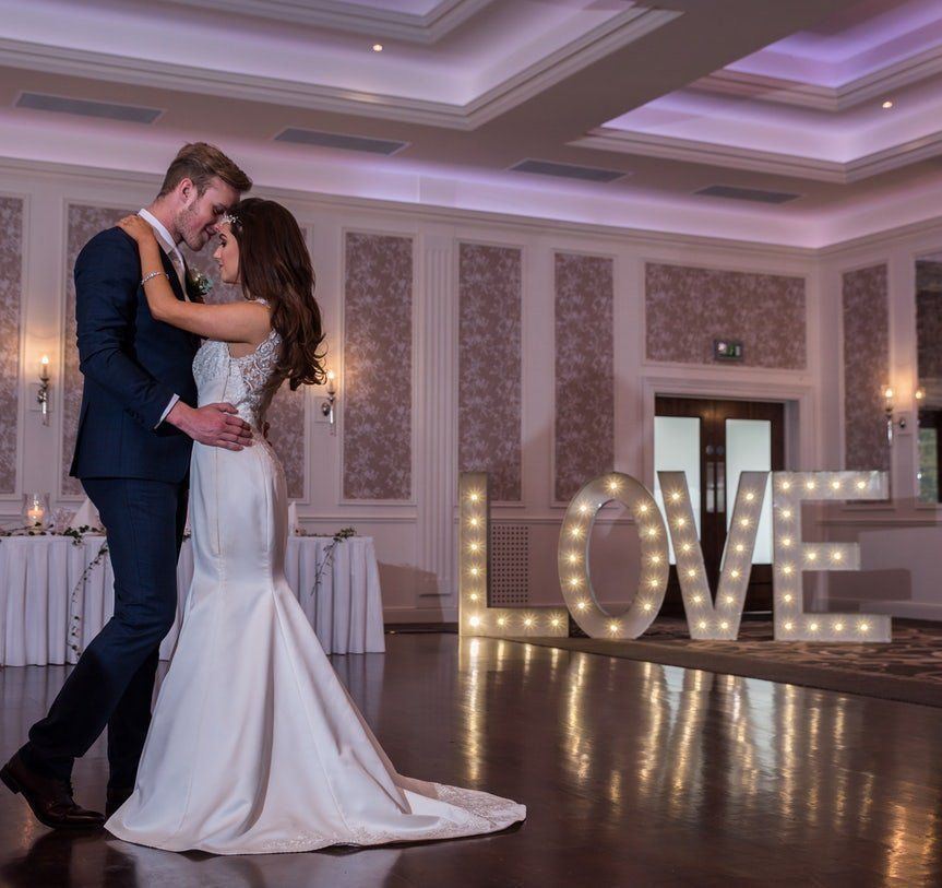 Couple dancing in a ballroom beside illuminated “LOVE” letters on the floor