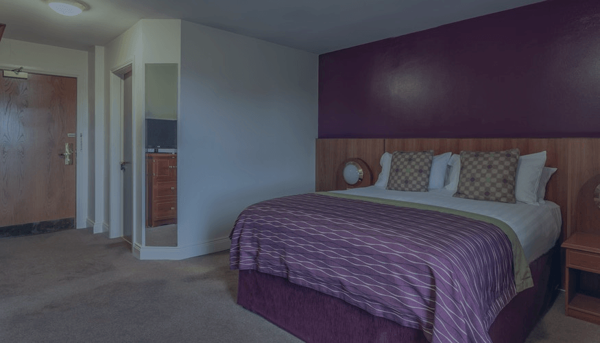 Hotel room with purple accent wall and bed, dresser, and hallway entrance